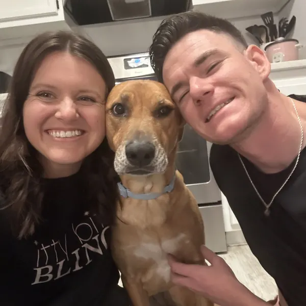 Sheridan and Bryan smiling in a selfie with a tan dog between them